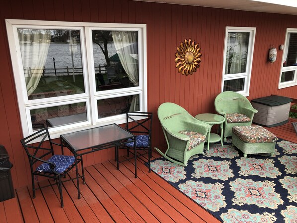 A covered outdoor seating area with a table and chairs, a decorative wall piece, and a patterned rug.