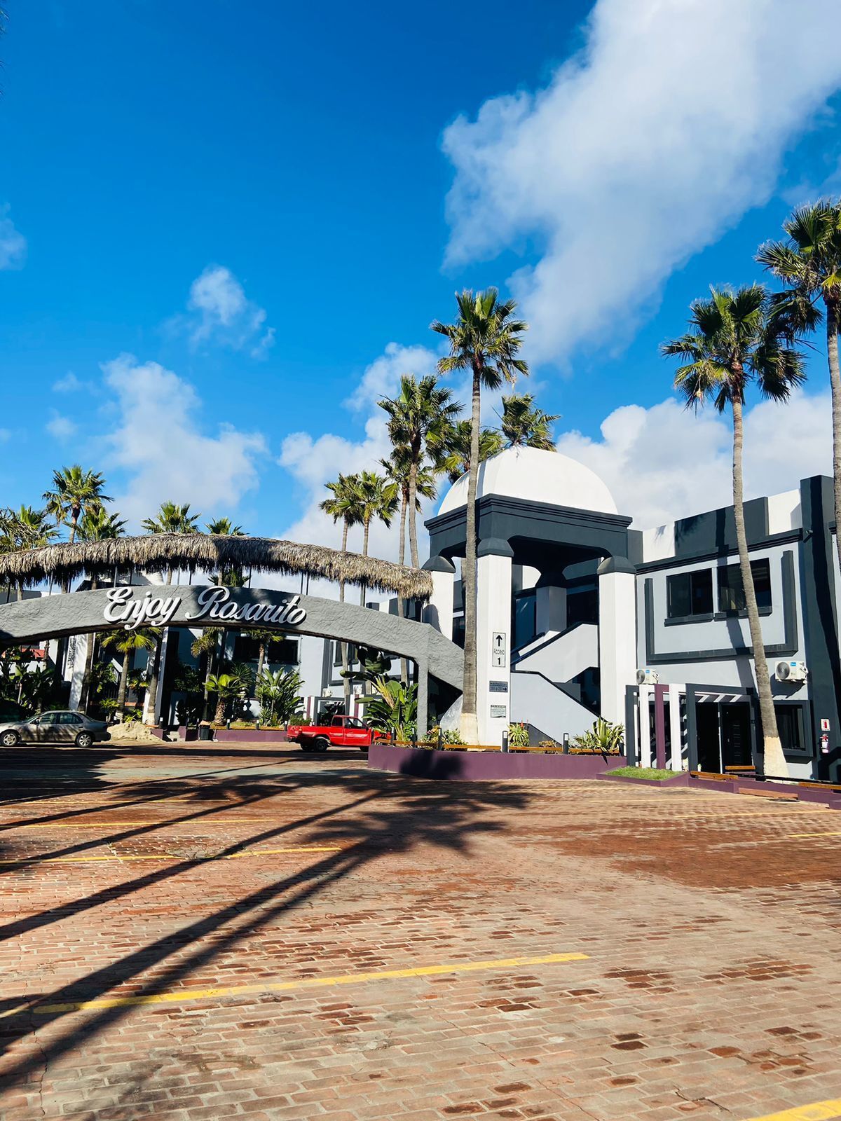Un edificio moderno con un letrero que dice "Enjoy Rasario" y palmeras al fondo.