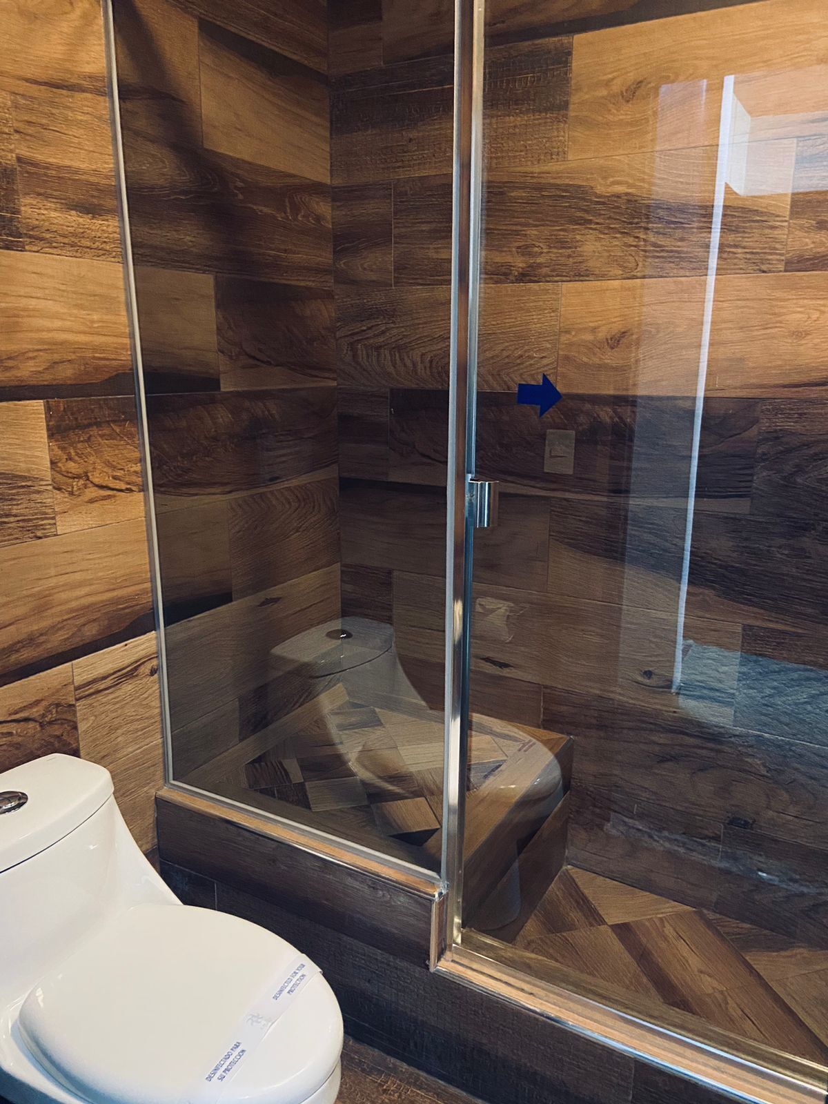 Un baño moderno con ducha de vidrio, suelo de madera y un inodoro blanco.