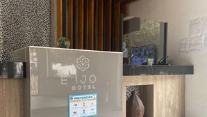 Zona de recepción de hotel con diseño moderno, que incluye suelo de mármol, paneles de madera y un mostrador con fachada de vidrio.