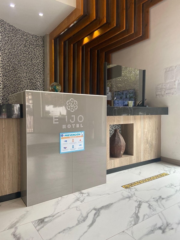 A hotel reception area with a modern design, featuring a marble floor, wooden paneling, and a glass-fronted counter. - Hotel Enjoy (Playas de Rosarito)