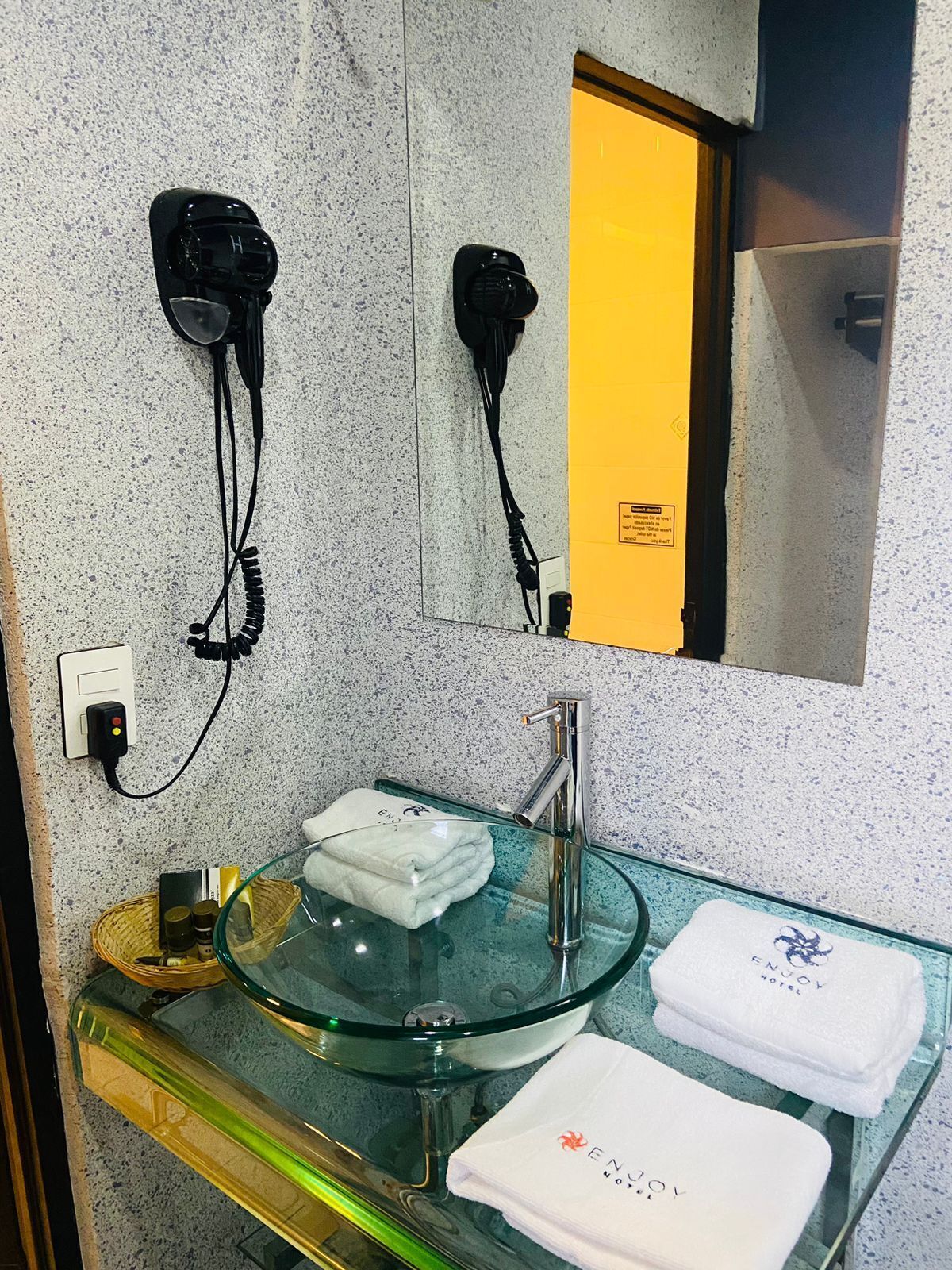 Ein Badezimmer mit einem Glaswaschbecken, einem Spiegel und zwei an der Wand befestigten Haartrocknern.