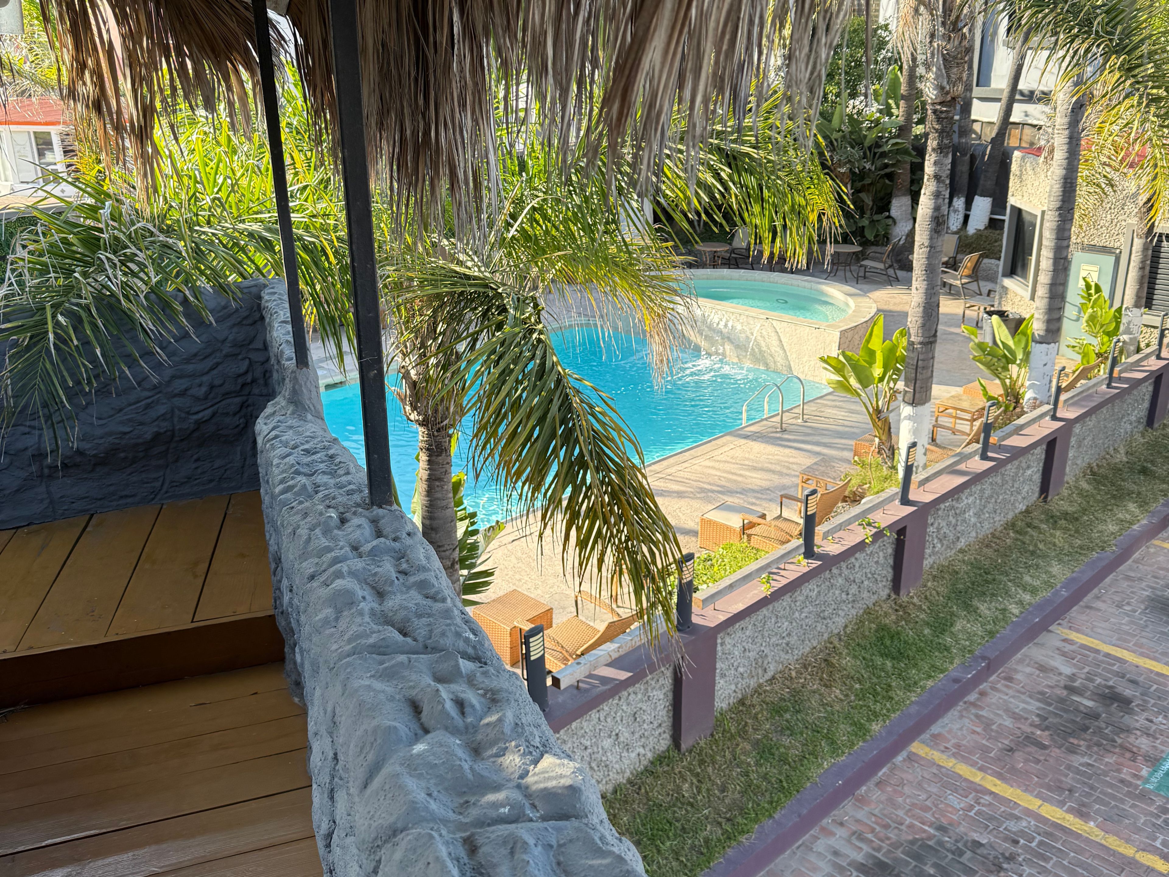 A pool area with a wooden deck, lounge chairs, and a stone wall.