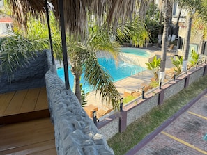 Zona de piscina con muelle de madera, sillones de descanso y pared de piedra.