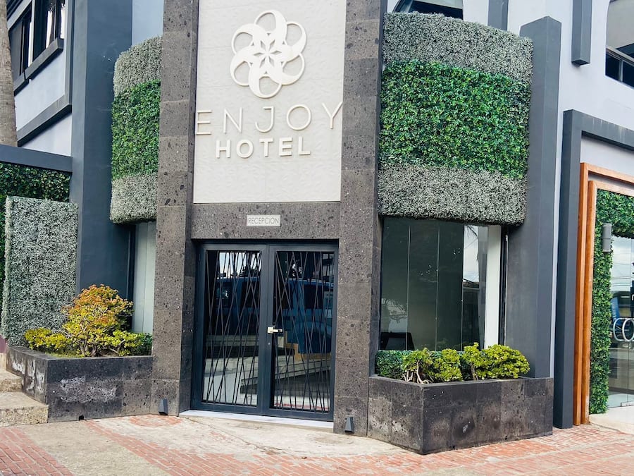 La entrada del HOTEL ENJOY con un diseño moderno, que incluye una zona de recepción y una puerta de cristal.