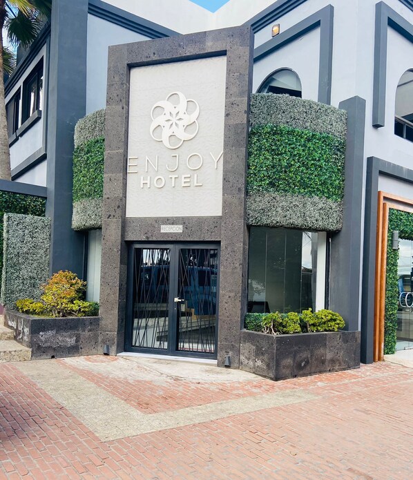 La entrada del HOTEL ENJOY con un diseño moderno, que incluye una zona de recepción y una puerta de cristal.