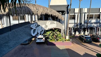 Entrada de hotel con un letrero grande, palmeras y coches estacionados.