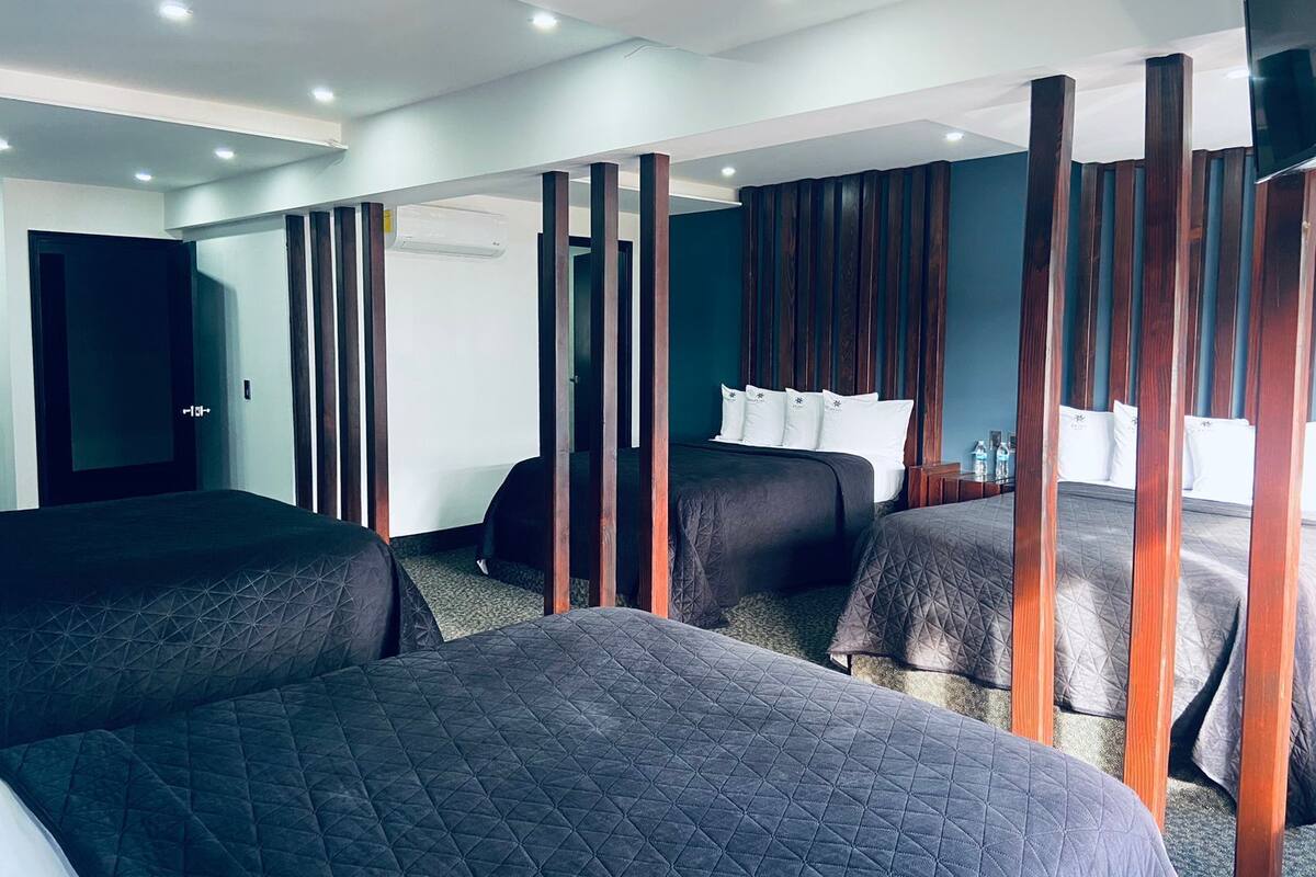A hotel room with two beds, a wooden partition, a flat-screen TV, and a door.