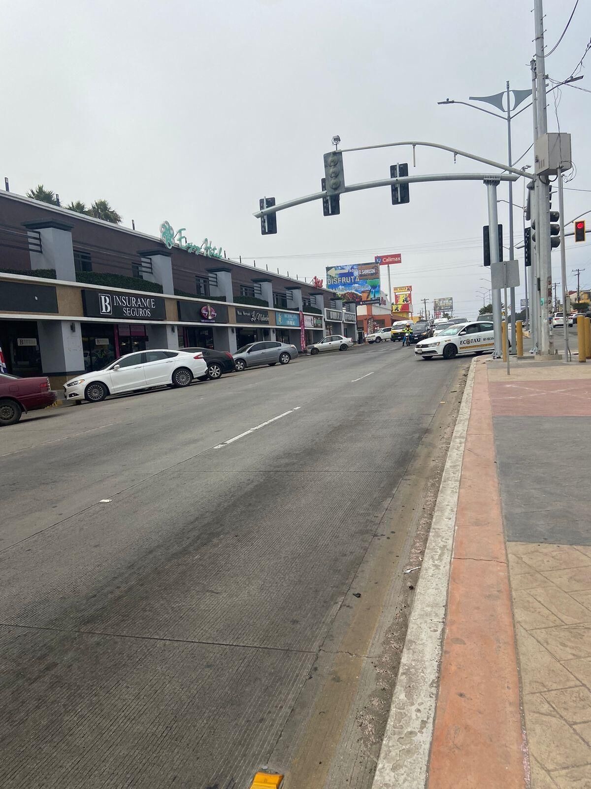 A street with cars parked on the side, a traffic light, and buildings with commercial signs.