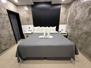 Habitación de hotel moderna con una cama grande, cabecera, dos mesitas de noche y una puerta.