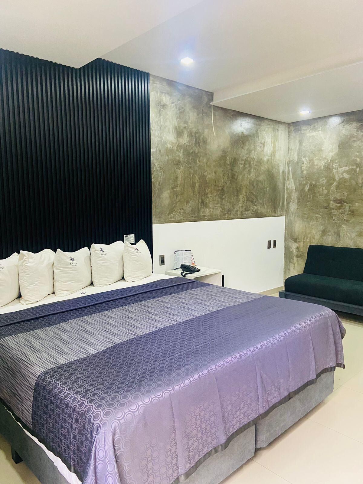 Een moderne slaapkamer met een groot bed, een donker hoofdbord, een grijze bank en een structuurwand.