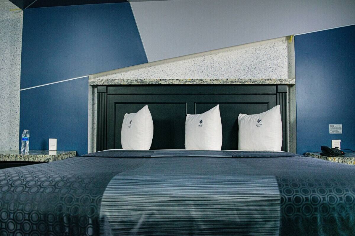 A modern hotel room with a large bed, three pillows, a marble headboard, and a granite countertop.