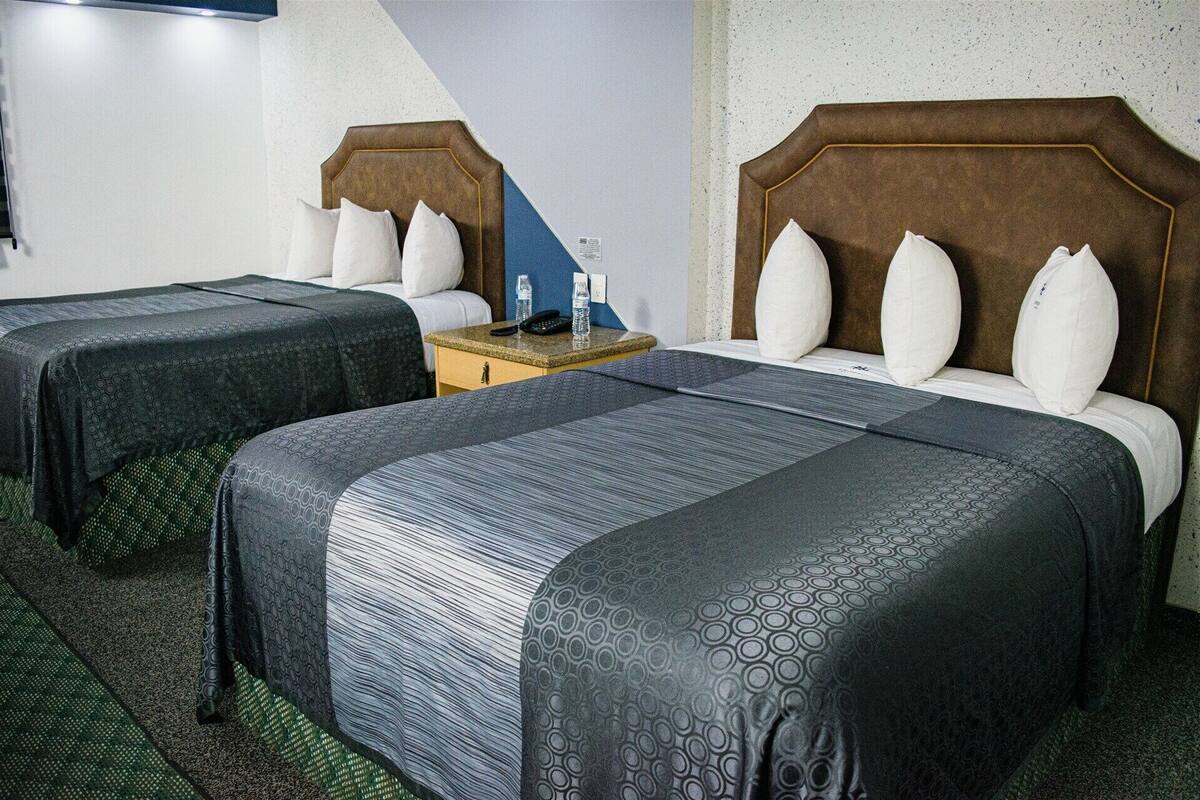 A hotel room with two beds, a nightstand, and a wall-mounted TV.