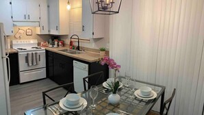 Une cuisine moderne avec des meubles blancs, une cuisinière et un lave-vaisselle. On y trouve une table à manger mise avec des assiettes, des verres et un vase rempli de fleurs.