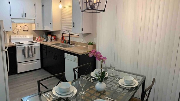 A modern kitchen with white cabinets, a stove, and a dishwasher. There is a dining table set with plates, glasses, and a vase with flowers. - 😍GREAT LOCATION 2BD/1BTH UNIT W/ PVT BACKYARD 😍 (Puyallup)