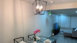 A dining area with a glass table set for four, a chandelier, and a living room in the background. - 😍GREAT LOCATION 2BD/1BTH UNIT W/ PVT BACKYARD 😍 (Puyallup)