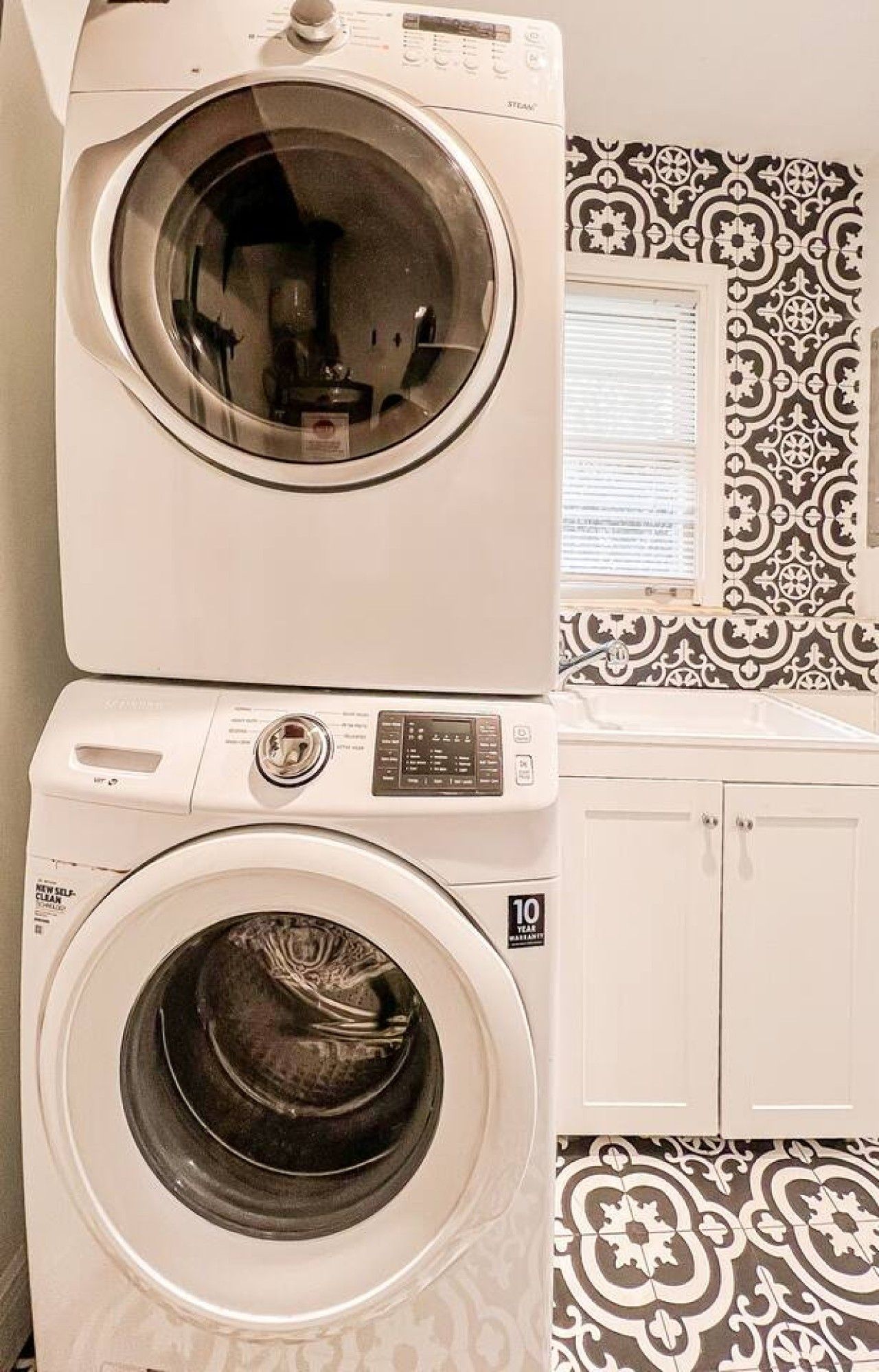 A laundry room with two front-loading washing machines, a sink, and patterned wall tiles.
