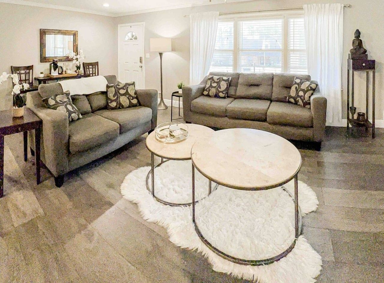 A living room with a sofa set, two round coffee tables, a dining table with chairs, and a lamp.