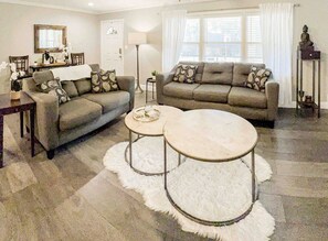 A living room with a sofa set, two round coffee tables, a dining table with chairs, and a lamp.