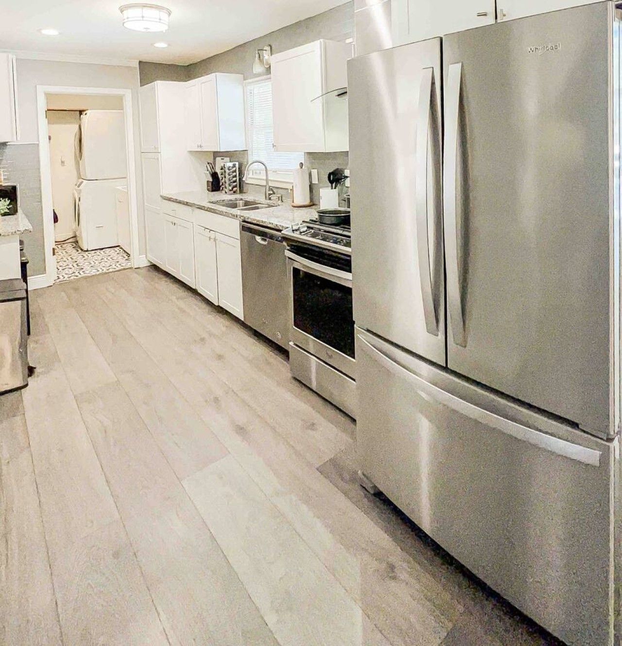 A modern kitchen with stainless steel appliances, white cabinetry, and a patterned floor.