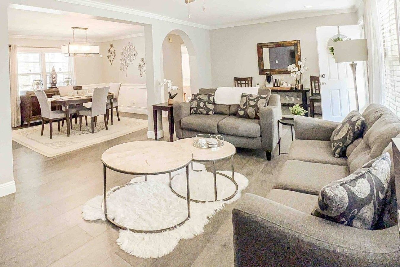 A modern living room with a sofa, two round coffee tables, and a dining area with chairs and a table.