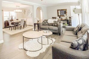 A modern living room with a sofa, two round coffee tables, and a dining area with chairs and a table. - In-Shower Sauna, Fenced Yard W/Deck & BBQ Near ATL (Atlanta)