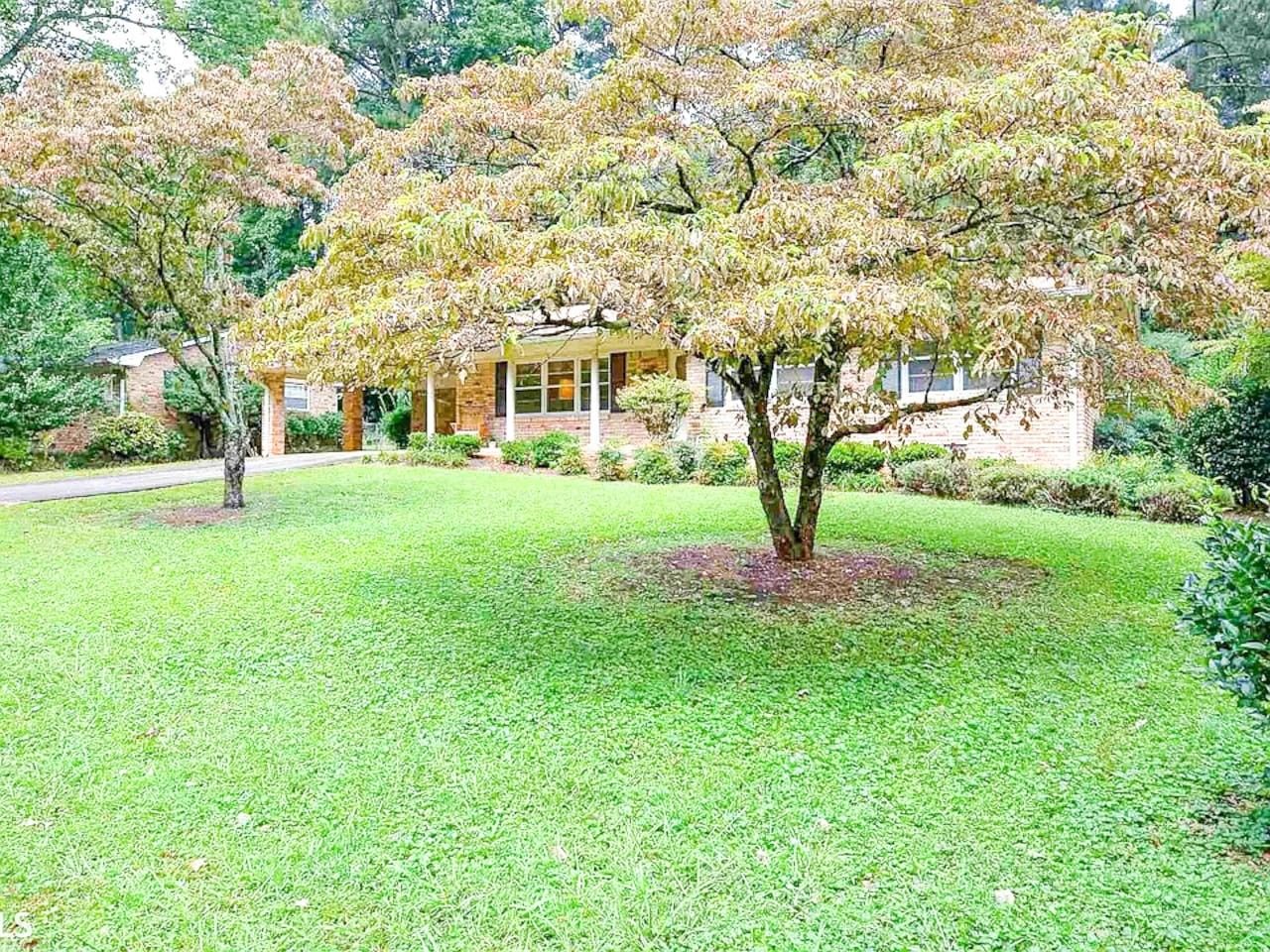 A residential area with a well-maintained lawn, a large tree, and a brick house with a window.
