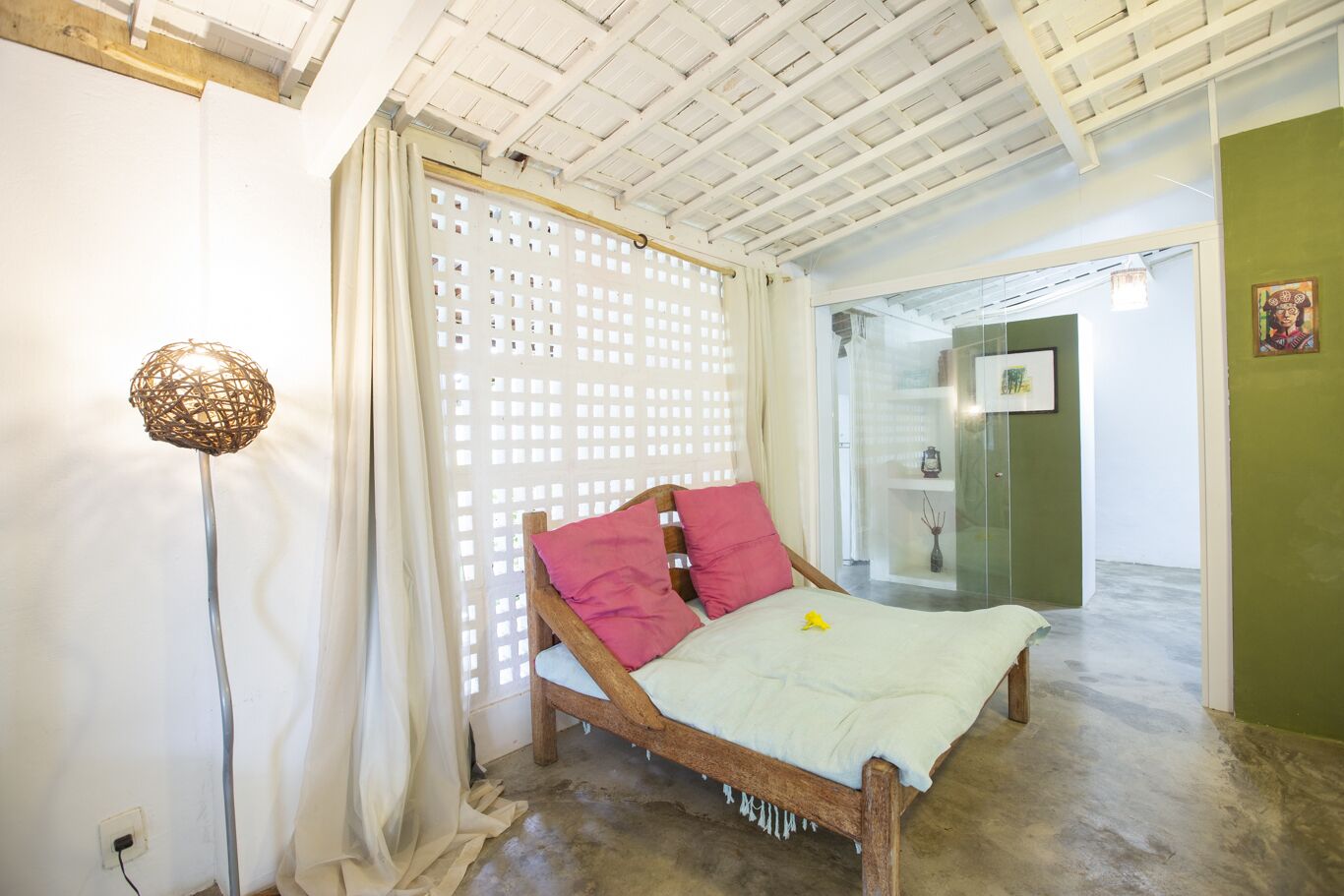 A bedroom with a wooden bed, a white curtain, a woven floor lamp, and a green wall.