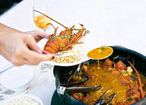A person serving a lobster with a bowl of rice and a pot of soup. - Villa Ostello Pousada (Paripueira)