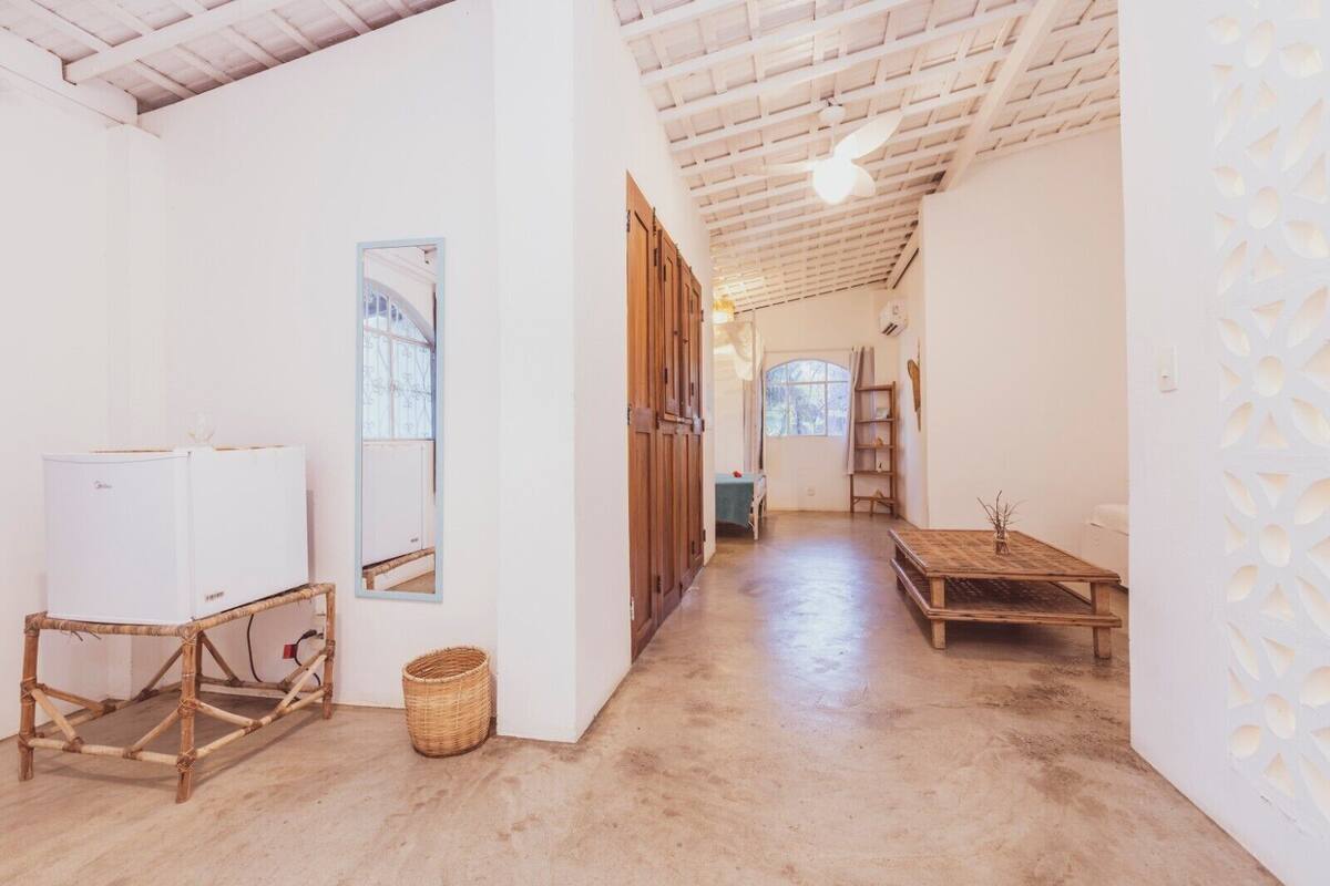 A spacious hallway with a wooden ceiling, a large mirror, a white refrigerator, a wicker basket, and a wooden table with a vase.