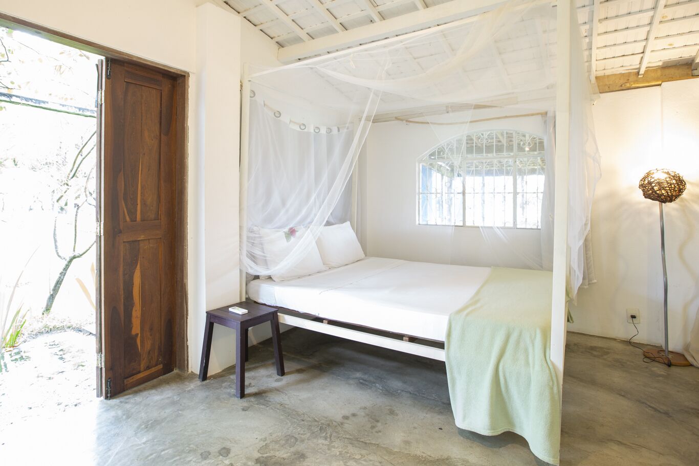 Una cama individual con dosel, una mesita de noche y una ventana con rejas.