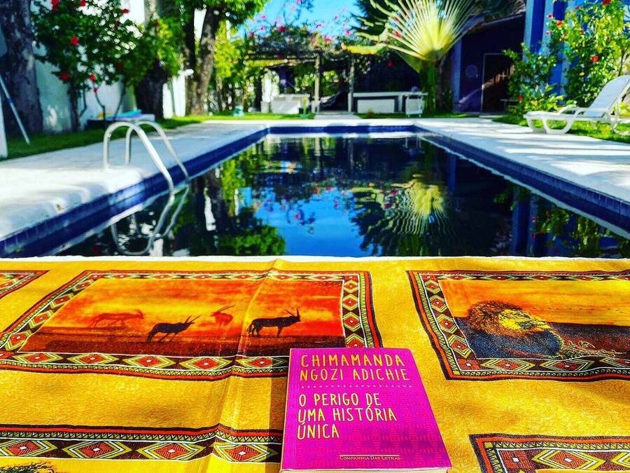 Vista de la piscina con un libro titulado "CHIMAMANDA NGOZI ADICHIE O PERIGO DE UMA HISTORIA" sobre un mantel estampado.