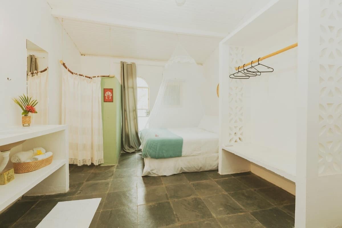 A room with a bed, a shelf with towels, a hanging shoe rack, and a door with a curtain.
