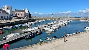 Uma marina com barcos atracados, um farol ao fundo e edifícios ao longo da orla.