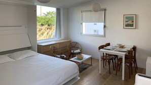 Quarto com cama, mesa de jantar com cadeiras, janela com vista para árvores e luminária no teto.