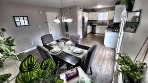 Un coin repas avec une table dressée pour quatre personnes, entourée de chaises, et une cuisine en arrière-plan.