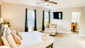 Une chambre à coucher avec un lit, une chaise, un téléviseur et un ventilateur de plafond.