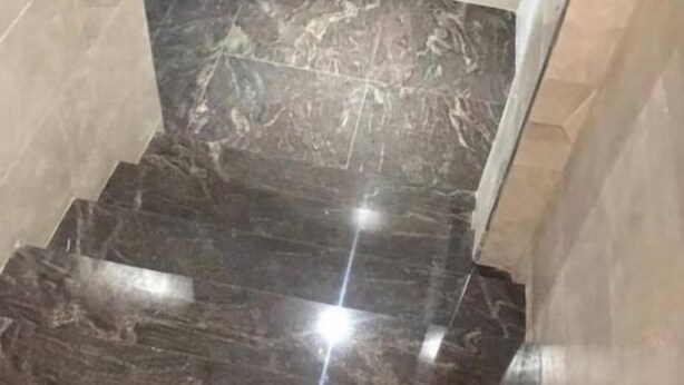 Ein Treppenhaus aus dunklem Marmor mit spiegelnder Oberfläche, das zu einer höheren Etage führt.