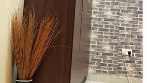 Ein Zimmer mit einem großen Holzschrank, einer Wand mit Backsteinmuster und einer Vase mit hohen Gräsern.