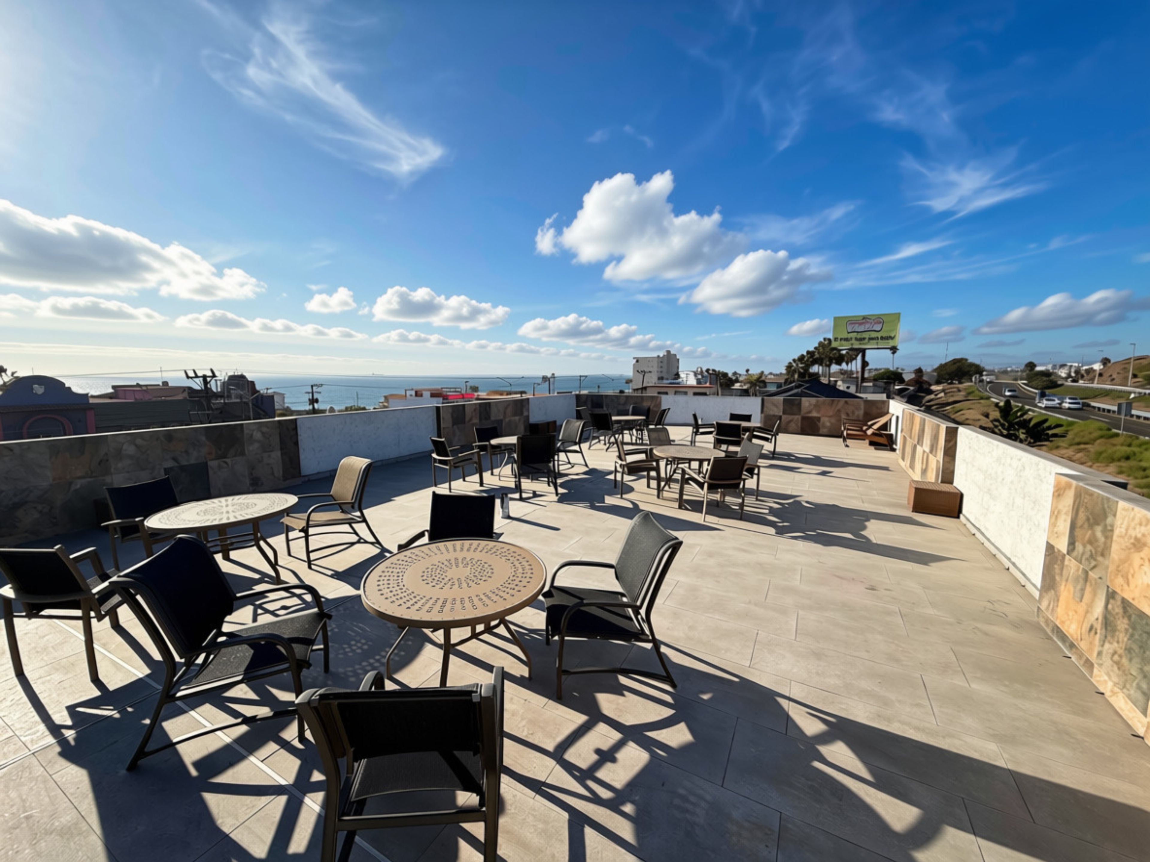Un espace extérieur aménagé avec des tables et des chaises, offrant une vue sur le paysage urbain et la mer.