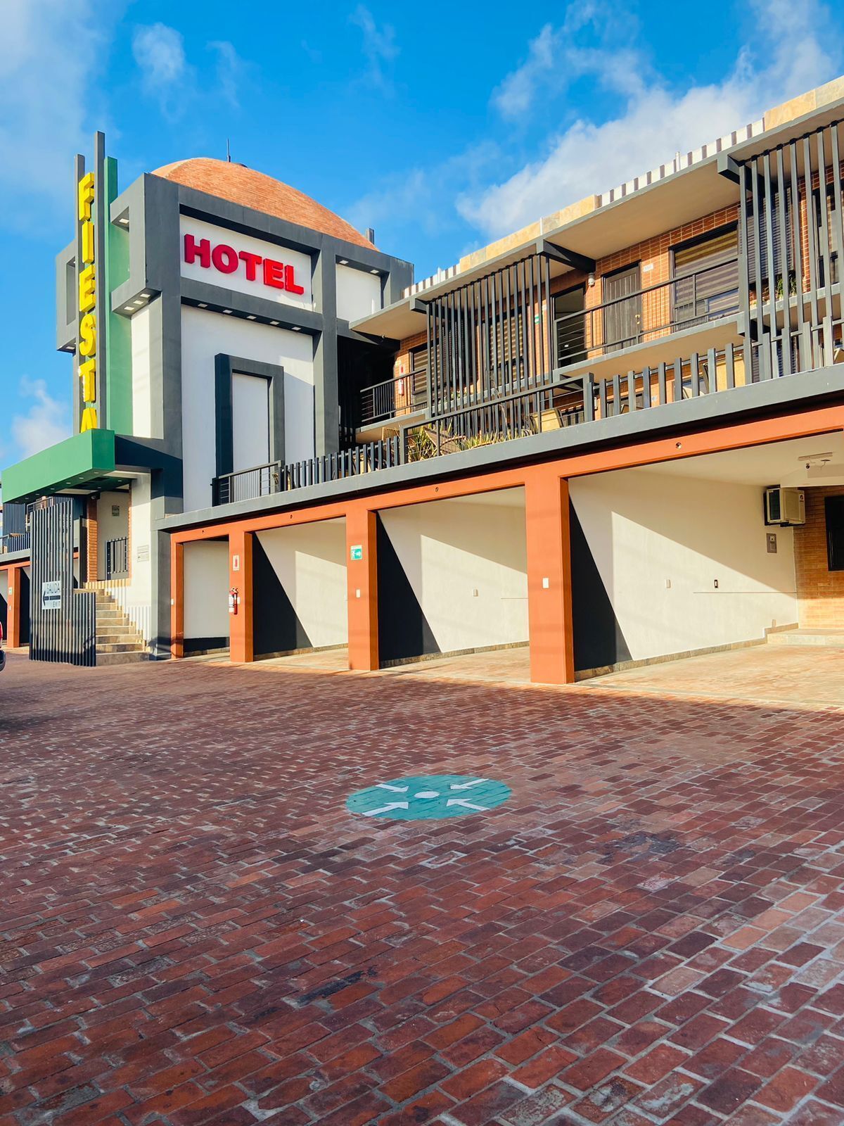A modern hotel with a prominent 'HOTEL' sign, a covered entrance, and a brick-paved courtyard.