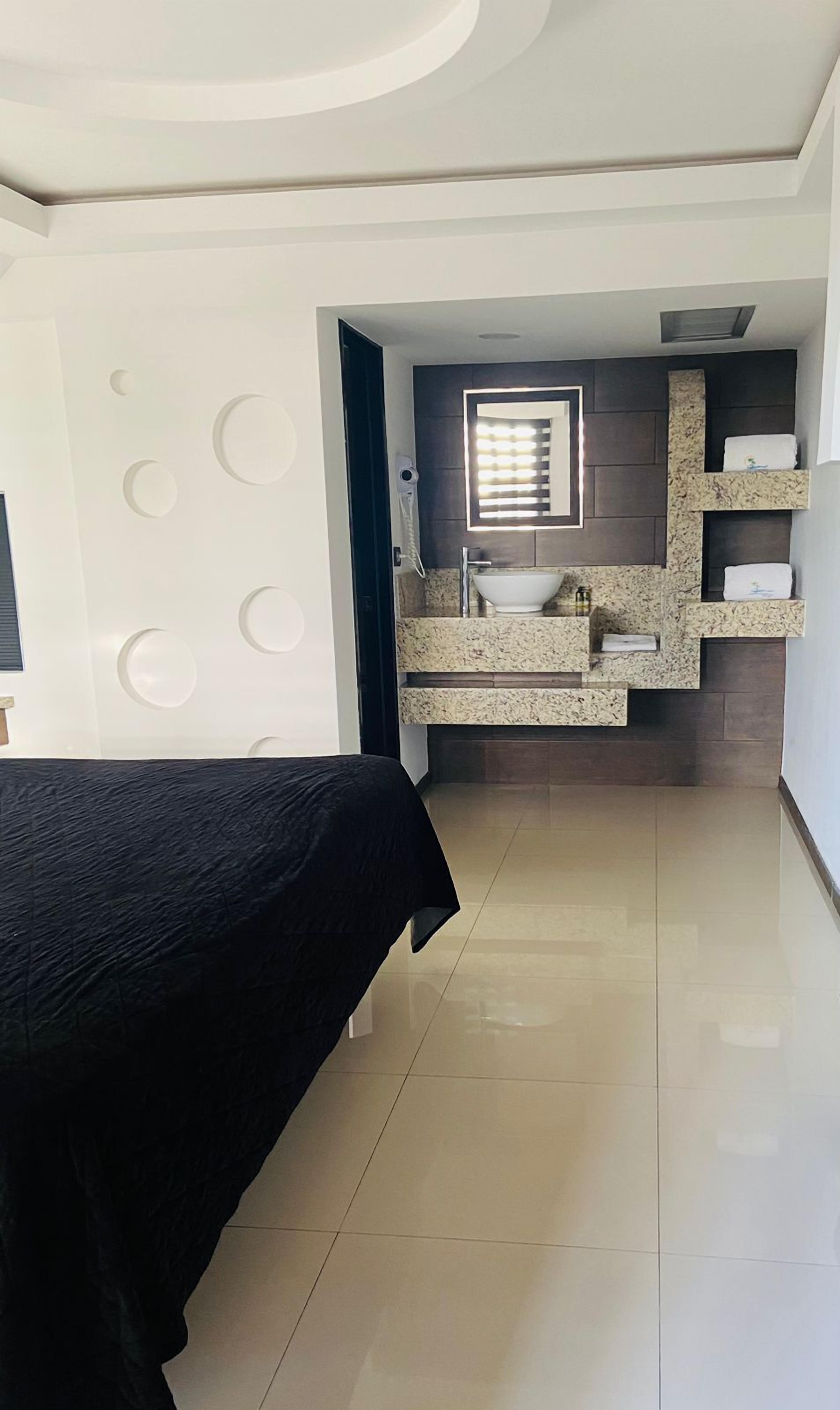 Un dormitorio moderno con cama, un baño con lavamanos y espejo, y un pasillo que conduce a otra habitación.