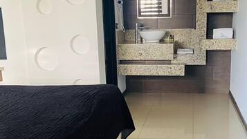 Un dormitorio moderno con cama, un baño con lavamanos y espejo, y un pasillo que conduce a otra habitación.