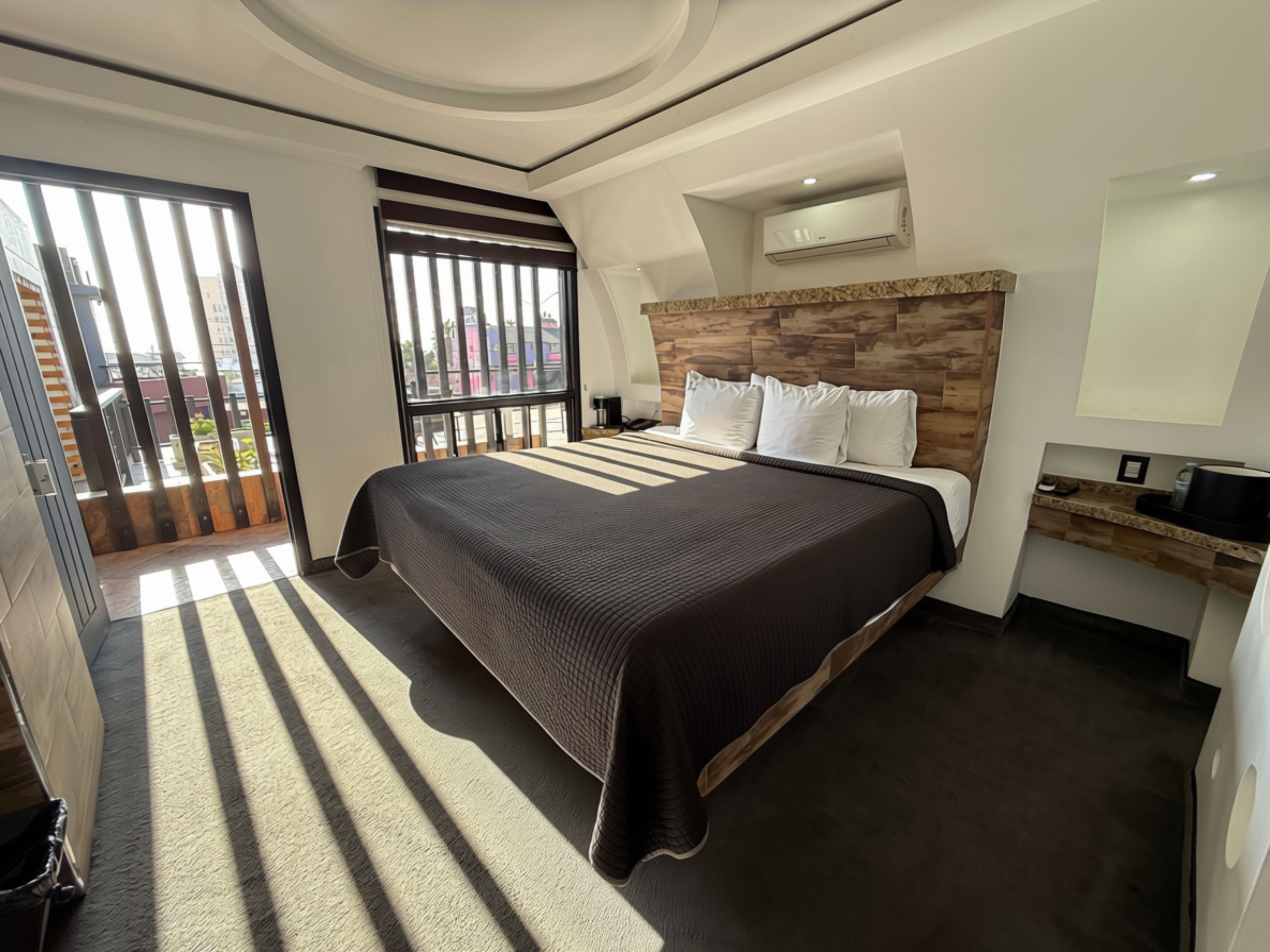 Una habitación de hotel moderna con una cama grande, un escritorio integrado, una ventana con persianas y un aire acondicionado instalado en el techo.