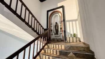 A staircase with a wooden handrail leading to a landing with a statue and a brick archway.