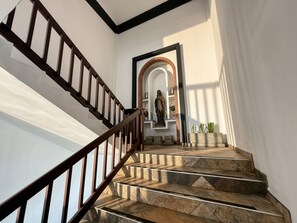 Una escalera con barandilla de madera que lleva a un rellano con una estatua y un arco de ladrillo.