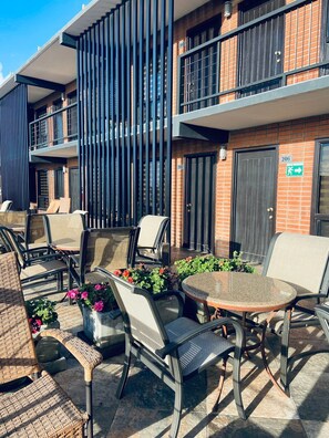 An outdoor seating area with wicker chairs and a round table, surrounded by potted plants and flowers. - Hotel Fiesta Rosarito (Playas de Rosarito)