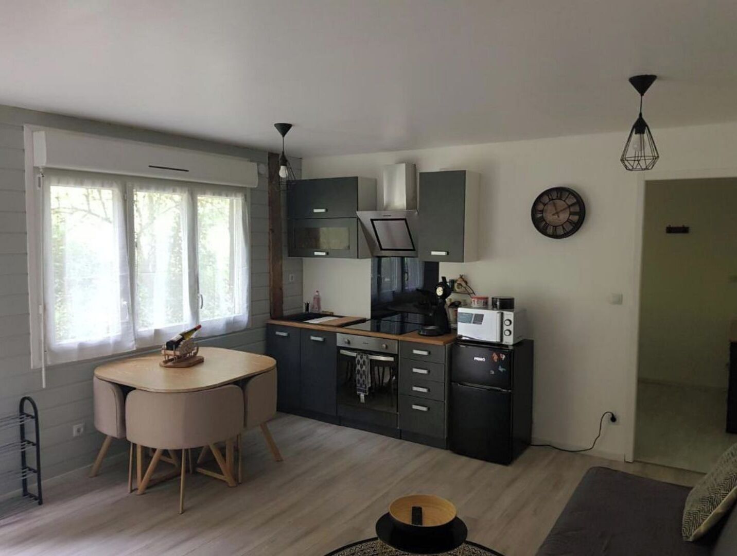 Cozinha moderna com armários escuros, micro-ondas e máquina de café. Há uma mesa de jantar com cadeiras e uma janela com cortinas.