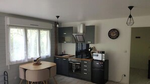 A modern kitchen with dark cabinets, a microwave, and a coffee maker. There is a dining table with chairs and a window with curtains.