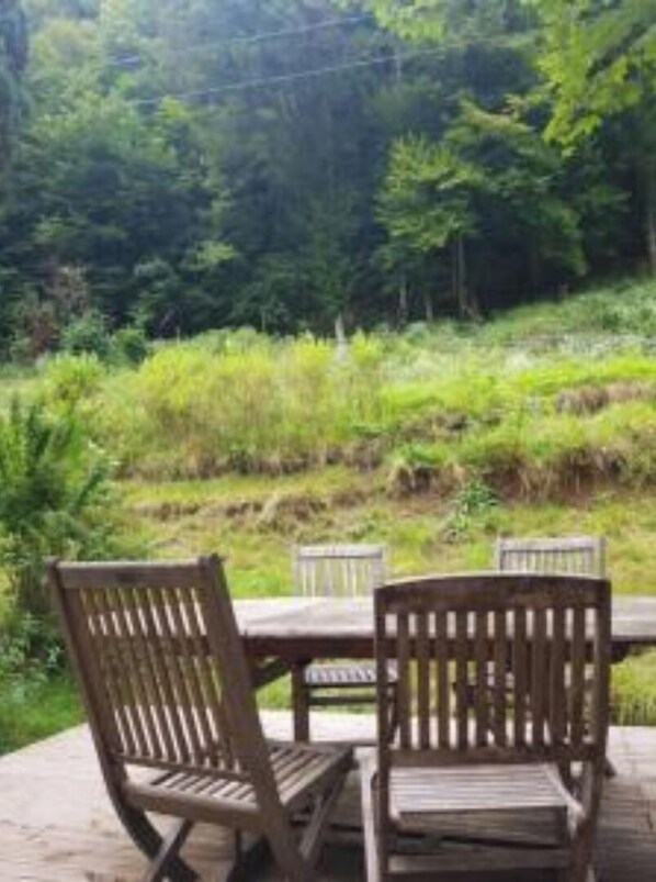 A wooden deck with two chairs and a table, surrounded by lush greenery.